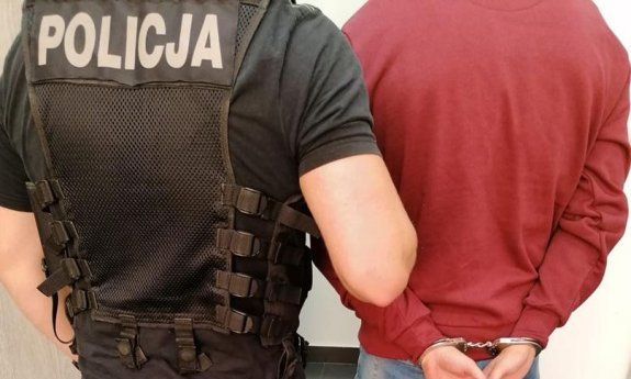policjant w kamizelce z napisem: Policja prowadzi zatrzymanego