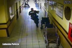 Policjant z dzieckiem na rękach biegnie po szpitalnym korytarzu&quot;&gt;