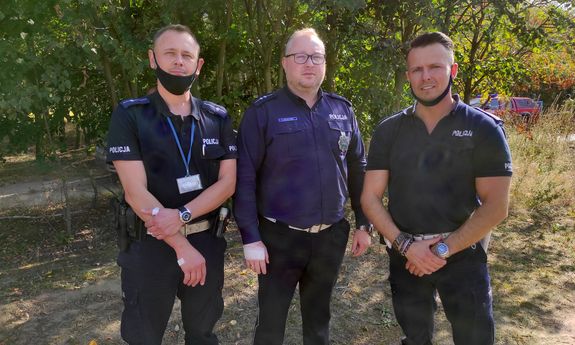 Trzej umundurowani policjanci stoją na dworze, w tle widać drzewa
