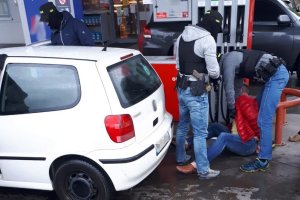 Policjanci przeszukują zatrzymanego mężczyznę siedzącego na ziemi na terenie stacji benzynowej