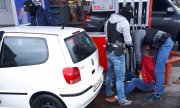 Policjanci przeszukują zatrzymanego mężczyznę siedzącego na ziemi na terenie stacji benzynowej