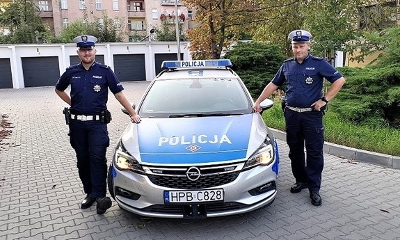 dwaj policjanci, którzy uratowali kobietę stoją obok radiowozu policyjnego