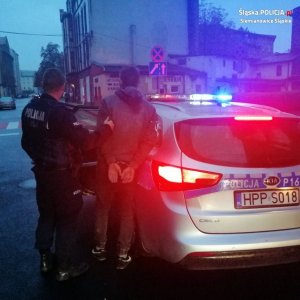 policjant stoi z zatrzymanym stoi przy radiowozie&quot;&gt;