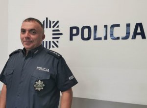 Policjant pozuje na tle napisu Policja