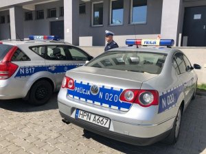 umundurowany policjant stoi pomiędzy dwoma oznakowanymi radiowozami