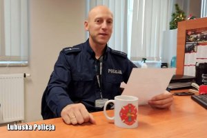 umundurowany policjant za biurkiem, w ręku trzyma pismo