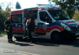 Policjantka z dzieciątkiem na ręku stoi przy ambulansie