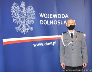 Na zdjęciu starszy sierżant Wiktor Fedorczuk stojący z odznaczeniem Brązowym Krzyżem Zasługi na tle baneru Wojewody Dolnośląskiego