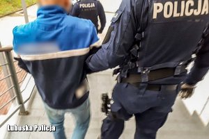 umundurowany policjant prowadzi zatrzymanego