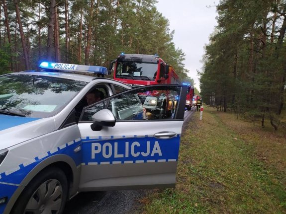 policjant w radiowozie na miejscu zdarzenia, za nim stoją dwa wozy strażackie