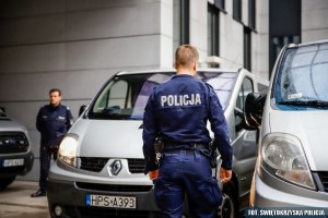 Policjanci stoją obok samochodów służących do transportu więźniów