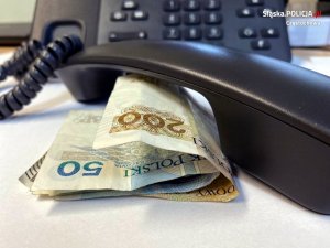 słuchawka telefonu leży na stoliku przy niej banknoty pieniędzy, w tle telefon z klawiaturą