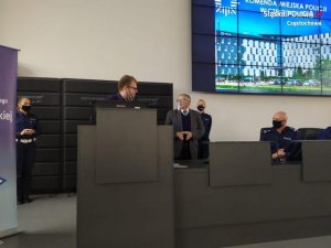 Prezes Związku Głuchych z tłumaczem języka migowego stoją przed mikrofonem na auli Komendy.