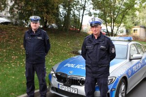 mł. asp. Daniel Szustakowski i asp. szt. Ireneusz Turek pozują do zdjęcia w mundurach na tle oznakowanego bmw