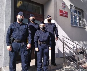 Na zdjęciu 3 miliccy policjanci i jedna policjantka biorący udział w akcji ratującej życie nieprzytomnej kobiety stojący na schodach przez budynkiem komendy policji