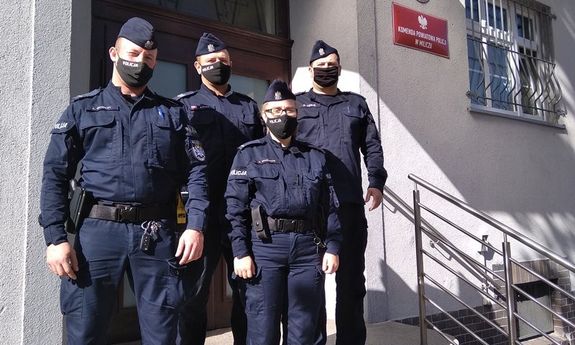 Na zdjęciu 3 miliccy policjanci i jedna policjantka biorący udział w akcji ratującej życie nieprzytomnej kobiety stojący na schodach przez budynkiem komendy policji