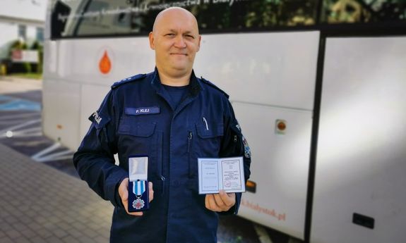 Policjant wraz z odznaką, który stoi przed krwiobusem
