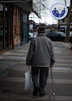 Zdjęcie przedstawia sylwetkę starszego mężczyzny idącego ulicą. W jednej ręce trzyma siatkę z zakupami, w drugiej laskę. Jest odwrócony tyłem. W prawym górnym rogu zdjęcia umieszczone zostało logo Centrum Poszukiwań Osób Zaginionych Komendy Głównej Policji