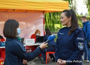 Dziennikarka w maseczce przeprowadzająca wywiad z policjantką, w tle osoby czekające na kwalifikację do oddania krwi