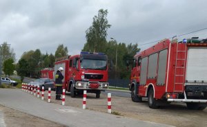 Dwa wozy strażackie, obok nich stoi strażak (bokiem, z pochyloną głową), z tyłu dwa radiwozy