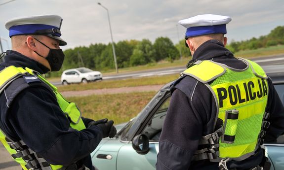 Umundurowani policjanci podczas kontroli drogowej stoją przy samochodzie