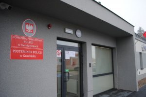 Fragment budynku Posterunku Policji w Grodzisku, na budynku wiszą dwie tablice informacyjne koloru czerwonego -na wyżej położonej jest napisane Komenda Powiatowa Policji w Siemiatyczach, na tej poniżej - Posterunek Policji w Grodzisku