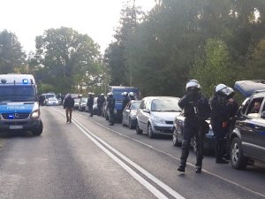 sznur aut stojących na pasie jezdni i policjanci w hełmach i kamizelkach kontrolują kierowców