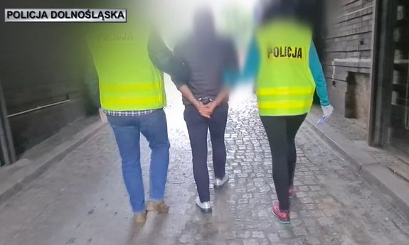 dwaj policjanci w żółtych kamizelkach prowadzą zatrzymanego