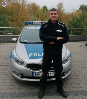 umundurowany policjant stoi przed maską radiowozu