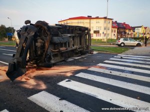 Na zdjęciu widać samochód ciężarowy przewrócony na prawy bok leżący na pasach na skrzyżowaniu. W dali widać samochód osobowy w który uderzył kierowca samochodu ciężarowego i policjantów oglądających pojazd