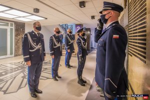 Komendant Główny Policji wraz z Zastępcami stoją przed tablicą pamięci i oddają hołd poległym policjantom. Na pierwszym planie policjant pełniący wartę honorową.