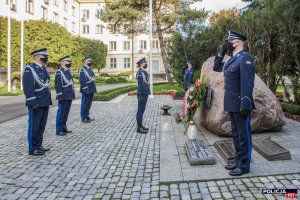 Obelisk „Poległym Policjantom - Rzeczpospolita Polska” przed budynkiem Komendy Głównej Policji. Przed obeliskiem stoją: Komendant Główny Policji wraz z Zastępcami - oddają hołd poległym policjantom. Na pierwszym panie policjant trzymający wartę honorową.