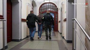 Dwaj nieumundurowani policjanci prowadzą podejrzanego korytarzem sądu