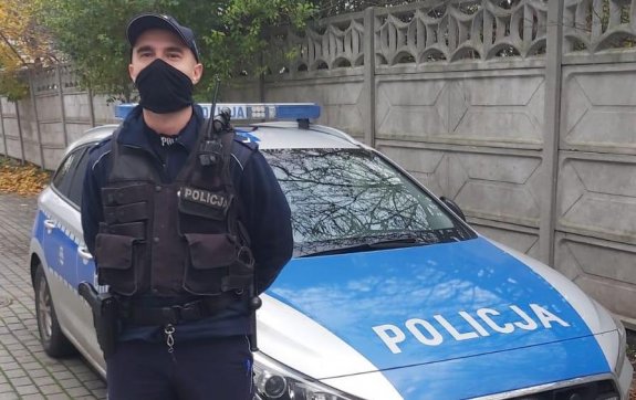 policjant w moro i w maseczce na twarzy stoi przed radiowozem