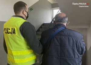 policjant prowadzi zatrzymanego  mężczyznę, w tle schody