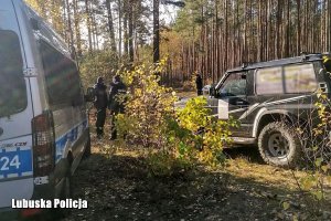 funkcjonariusze podczas poszukiwań w lesie, obok radiowóz i samochód terenowy