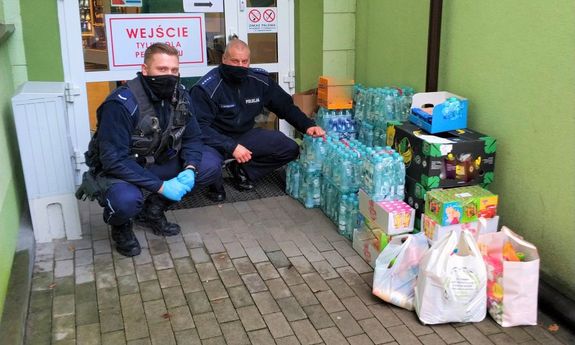 Policjanci pod drzwiami szpitala obok stoją artykuły spożywcze