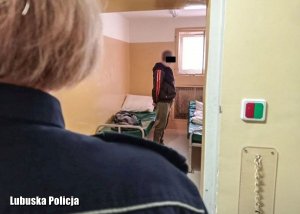 Policjantka, a w w tle pomieszczenie dla osób zatrzymanych i stojący mężczyzna