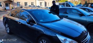 Na zdjęciu widoczny odzyskany pojazd marki Peugeot. Nad pojazdem stoi policjant ubrany w granatowy mundur wyjściowy i kurtkę z napisem Policja.