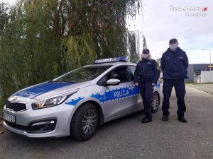 policjant i policjantka stoją przy radiowozie