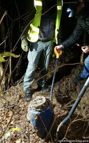 Na zdjęciu policjanci w środku nocy w lesie wyciągnęli niebieską beczkę.