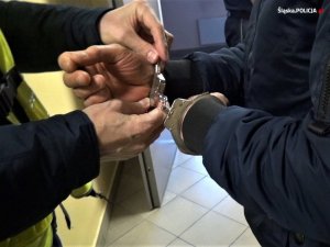 policjant zakłada kajdanki zatrzymanemu mężczyźnie