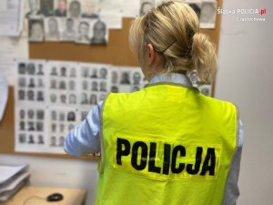 policjantka w kamizelce odblaskowej stoi przodem do tablicy z wizerunkami osób poszukiwanych
