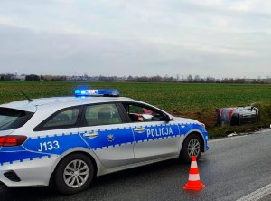 na pierwszym planie radiowóz policyjny na drodze, w tle samochód w rowie