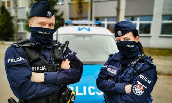 policjant i policjantka stojący przed radiowozem