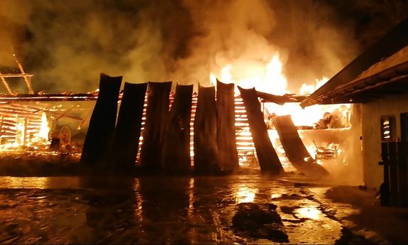 Płonąca stodoła. Widoczne buchajace w niebo połomienie dymoraz palące sie elemety drewniane. Poprawej stronie zarys zabudowań gospodarczych