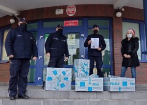 Policjanci i pracownicy Policji stoją na schodach Komendy Miejskiej Policji w Bydgoszczy. Przed nimi leżą paczki z darami dla dzieci ze szpitala