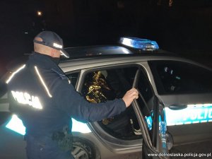 Na zdjęciu bezdomny siedzący w radiowozie, obok stoi policjant