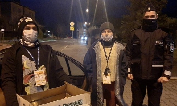 Na zdjęciu policjant z dwoma wolontariuszami. Wolontariusz trzyma karton w prezentami