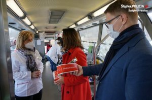 Na zdjęciu wnętrze autobusu. Na zdjęciu widać zastępcę szefa świętochłowickiej Policji oraz Prezydenta Miasta Świętochłowice w chwili odbioru z rąk pracownicy Regionalnego Centrum Krwiodawstwa i Krwiolecznictwa w Katowicach słodkich pakietów po oddaniu krwi